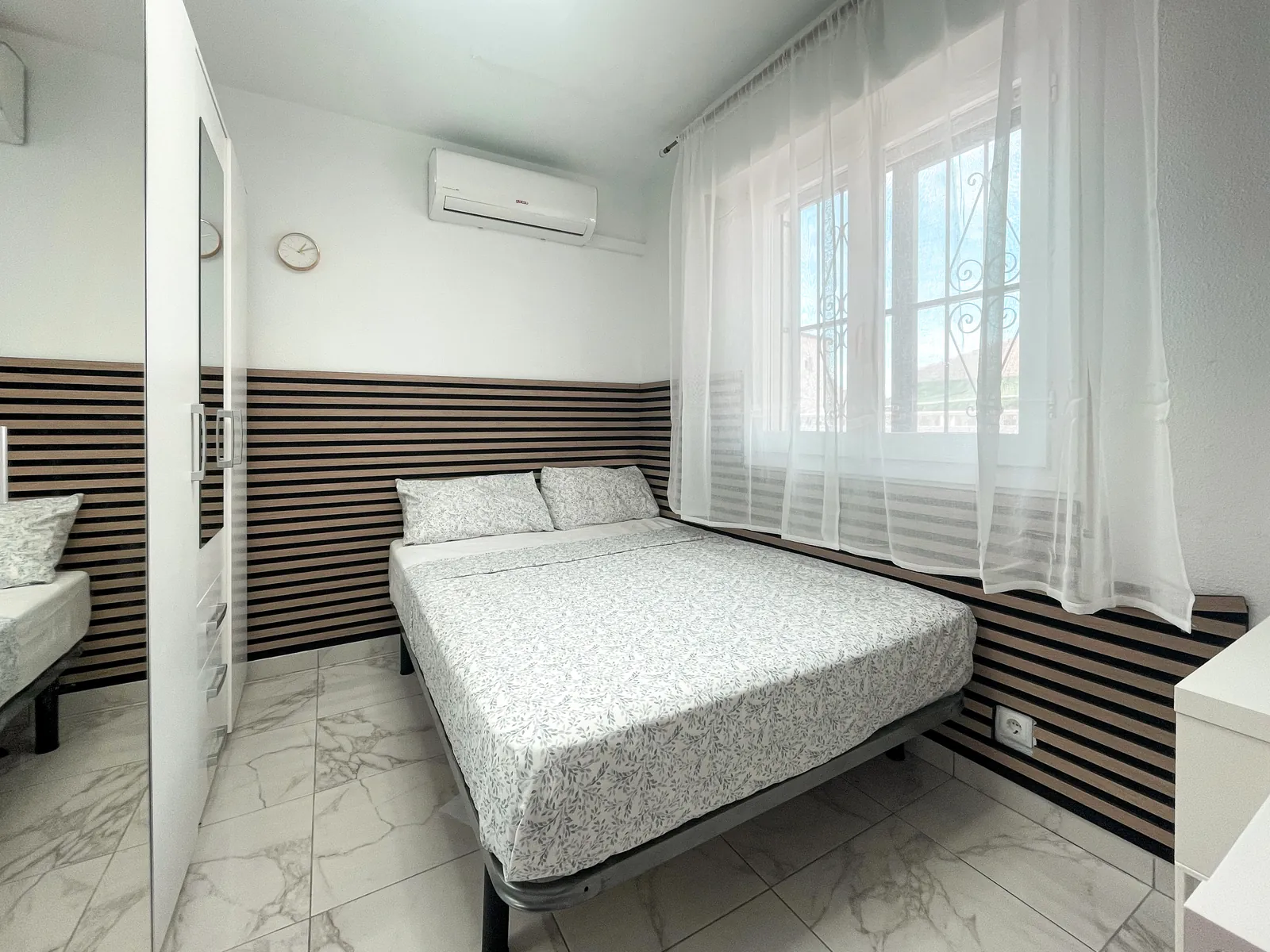 Double bed against a striped wooden wall panel, with air conditioning above the window